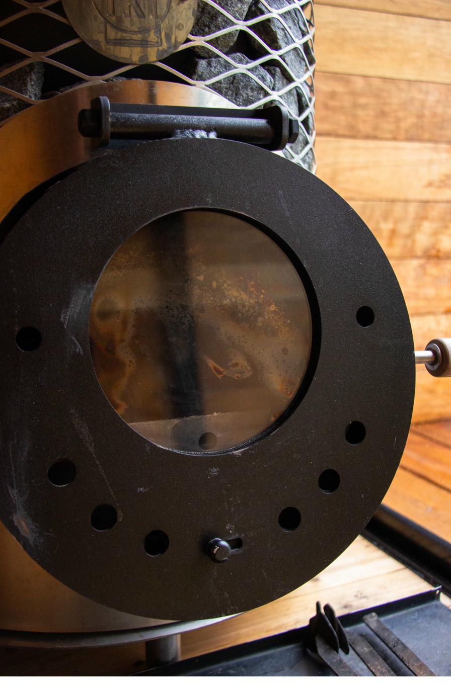 Glass firebox window of the Mini IKI wood-burning sauna stove showing flames