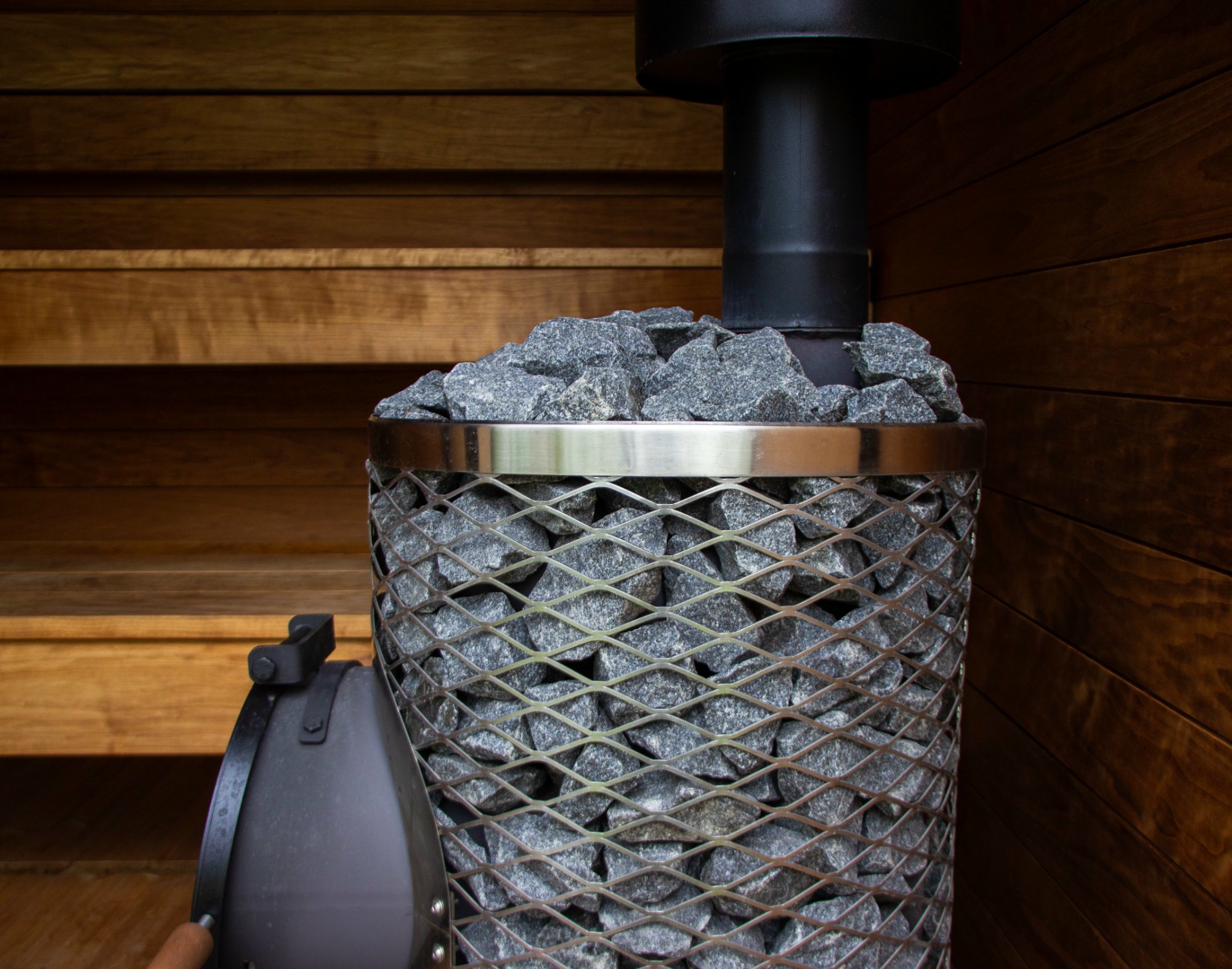Nahaufnahme des Mini IKI Holzofens mit Granitsteinen und Holzgriff, Sauna-Pflegedetail